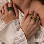 A close-up of hands wearing the Malachite Signet Ring and gold bands with a textured cream top. The vibrant green stone adds a bold, elegant touch to the look.
