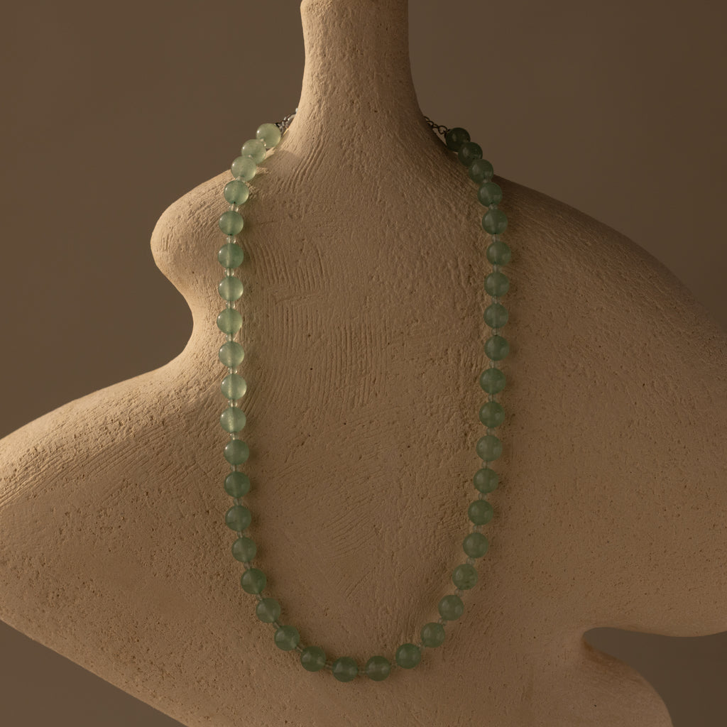 The Jade Choker Necklace in Silver is displayed on a textured, abstract beige bust set against a brown background.