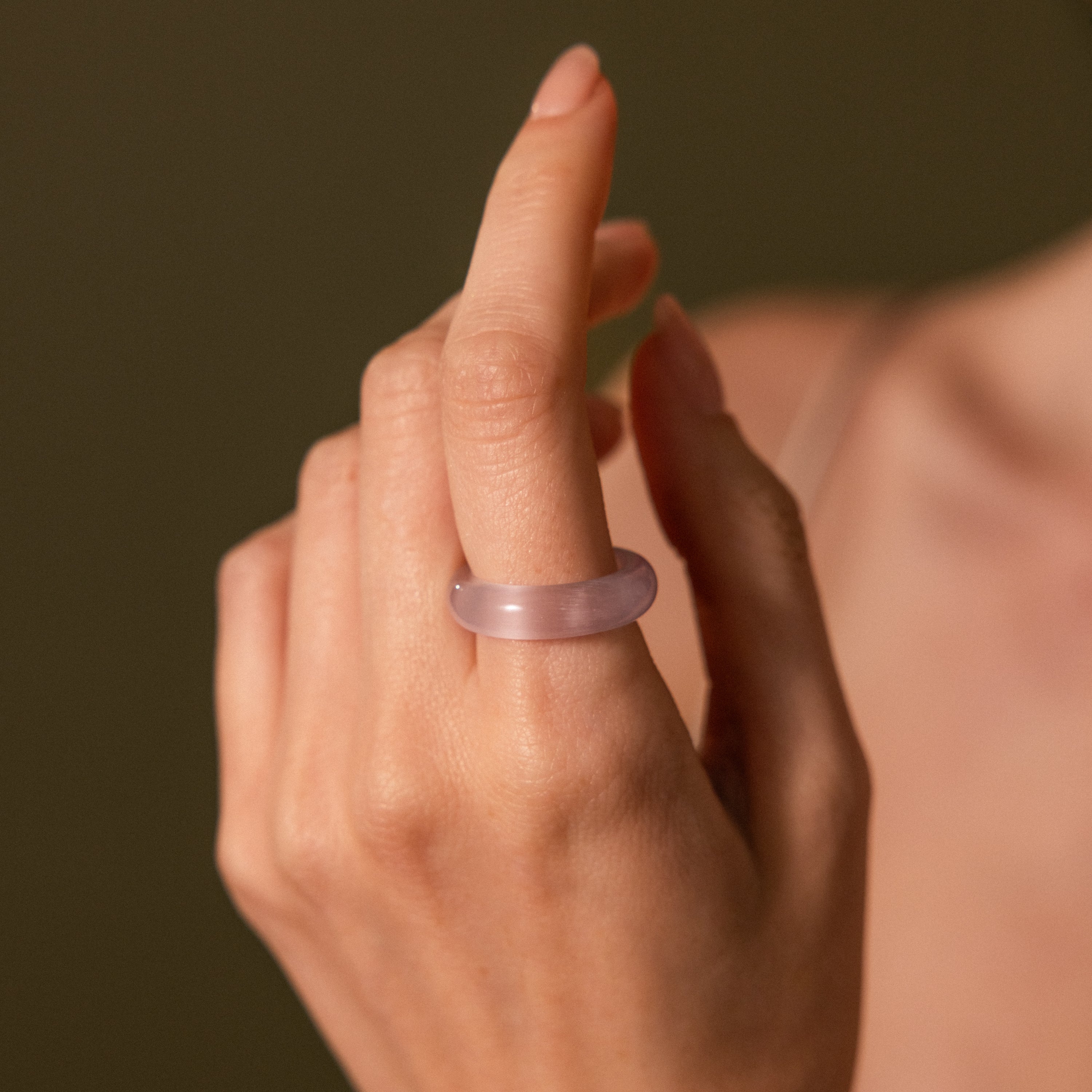 A hand with manicured nails wears the Skinny Lavender Jade Ring on the middle finger, its smooth, translucent look radiating calming energy.