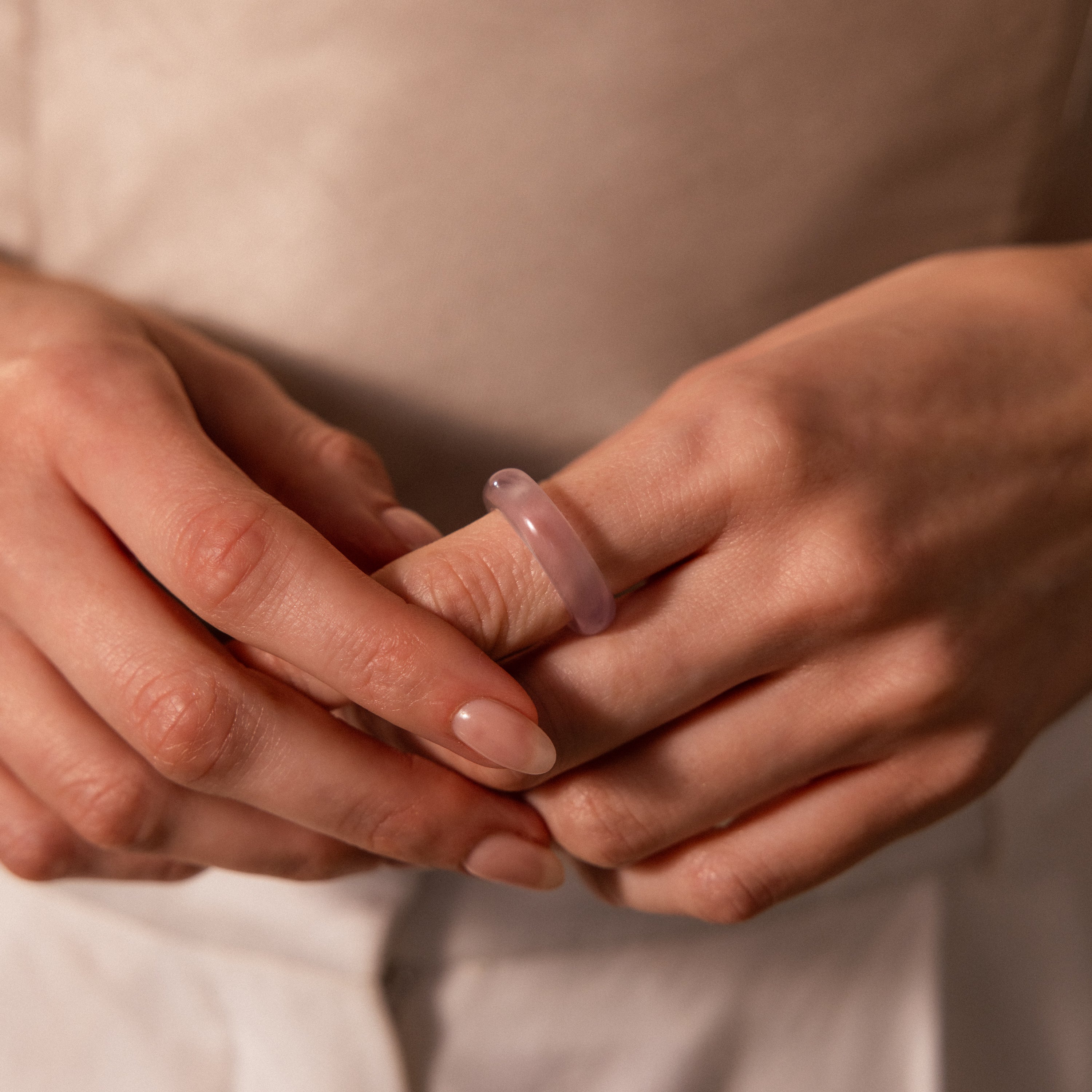 Hands with manicured nails wearing a Skinny Lavender Jade Ring, featuring a smooth, light purple hue on the middle finger, radiating calming energy.