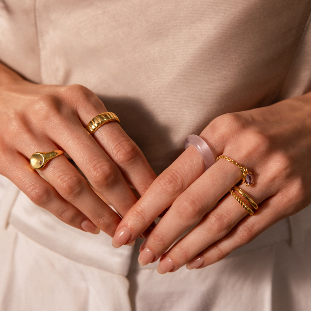 Close-up of manicured hands wearing gold stacking rings and the Skinny Lavender Jade Ring, exuding calming energy.