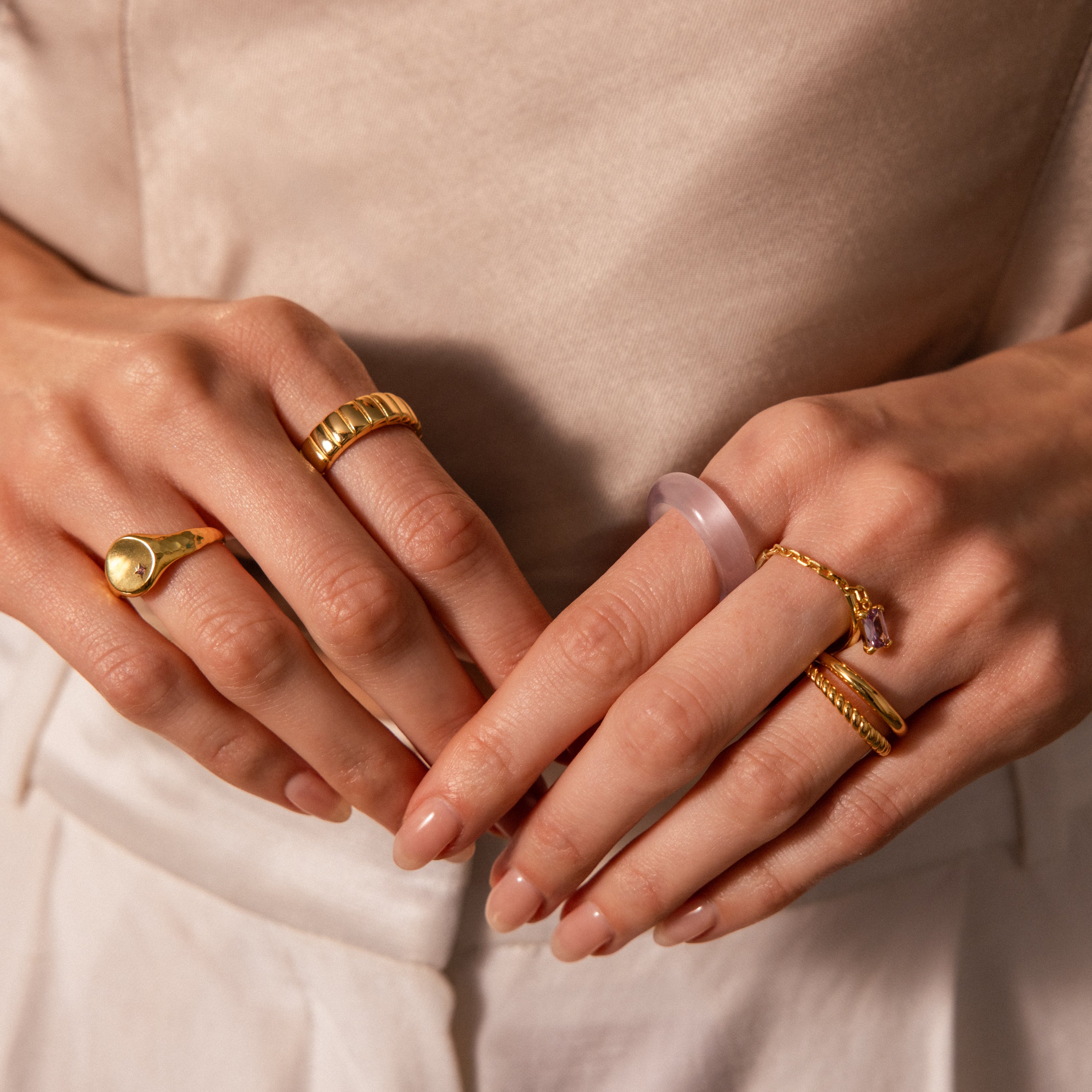 Close-up of manicured hands wearing gold stacking rings and the Skinny Lavender Jade Ring, exuding calming energy.