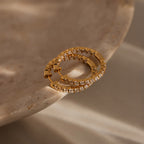 The Inside Out Diamond Hoops in 18K Gold, featuring clear stones in a classic huggie design, are displayed elegantly on a smooth beige marble surface.