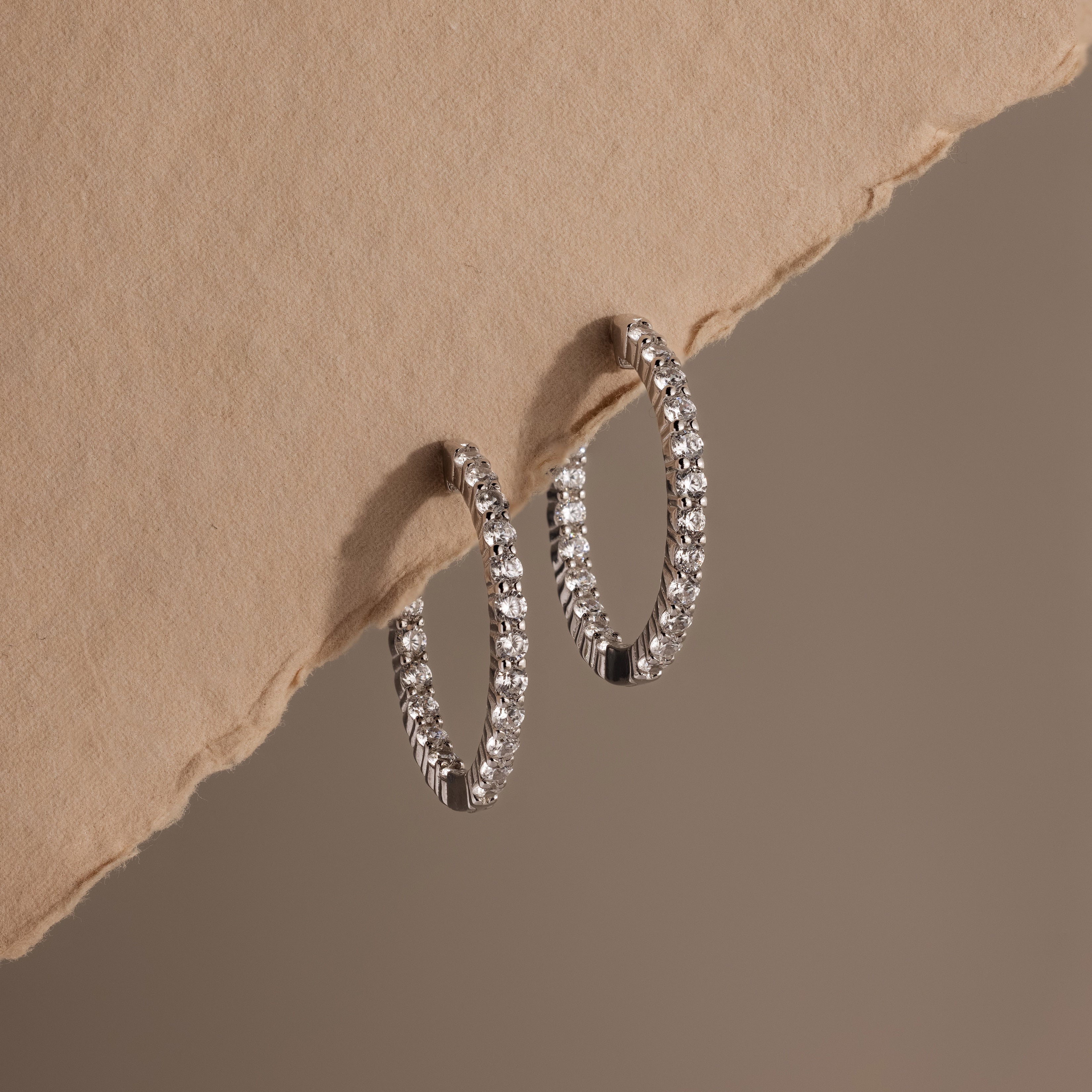 Inside Out Diamond Hoops in Silver displayed on a textured beige surface, casting soft shadows.