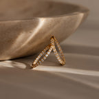 The Inside Out Diamond Hoops in 18K Gold, featuring sparkling diamonds and a timeless huggie design, are displayed against a beige stone bowl in gentle sunlight.