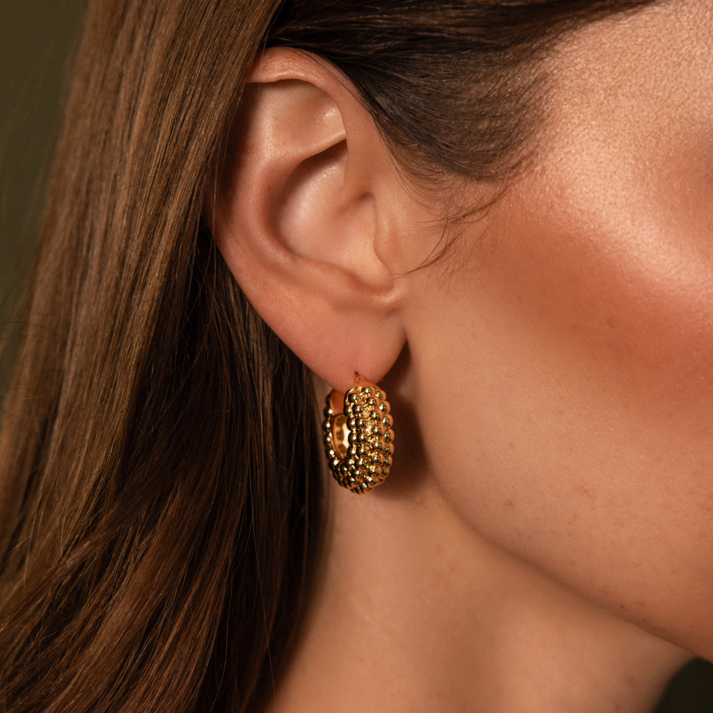 Close-up of a woman's ear wearing Beaded Dome Hoops in 18K Gold, showcasing textured gold beading, with smooth brown hair visible.