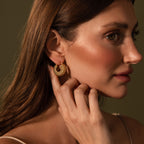 A woman with long brown hair touches Beaded Dome Hoops in 18K Gold, gazing to the side against a plain background.