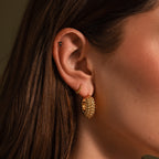 Close-up of a woman's ear adorned with three gold earrings, featuring statement hoops and Beaded Dome Hoops in 18K Gold with delicate beading in varying sizes and textures.