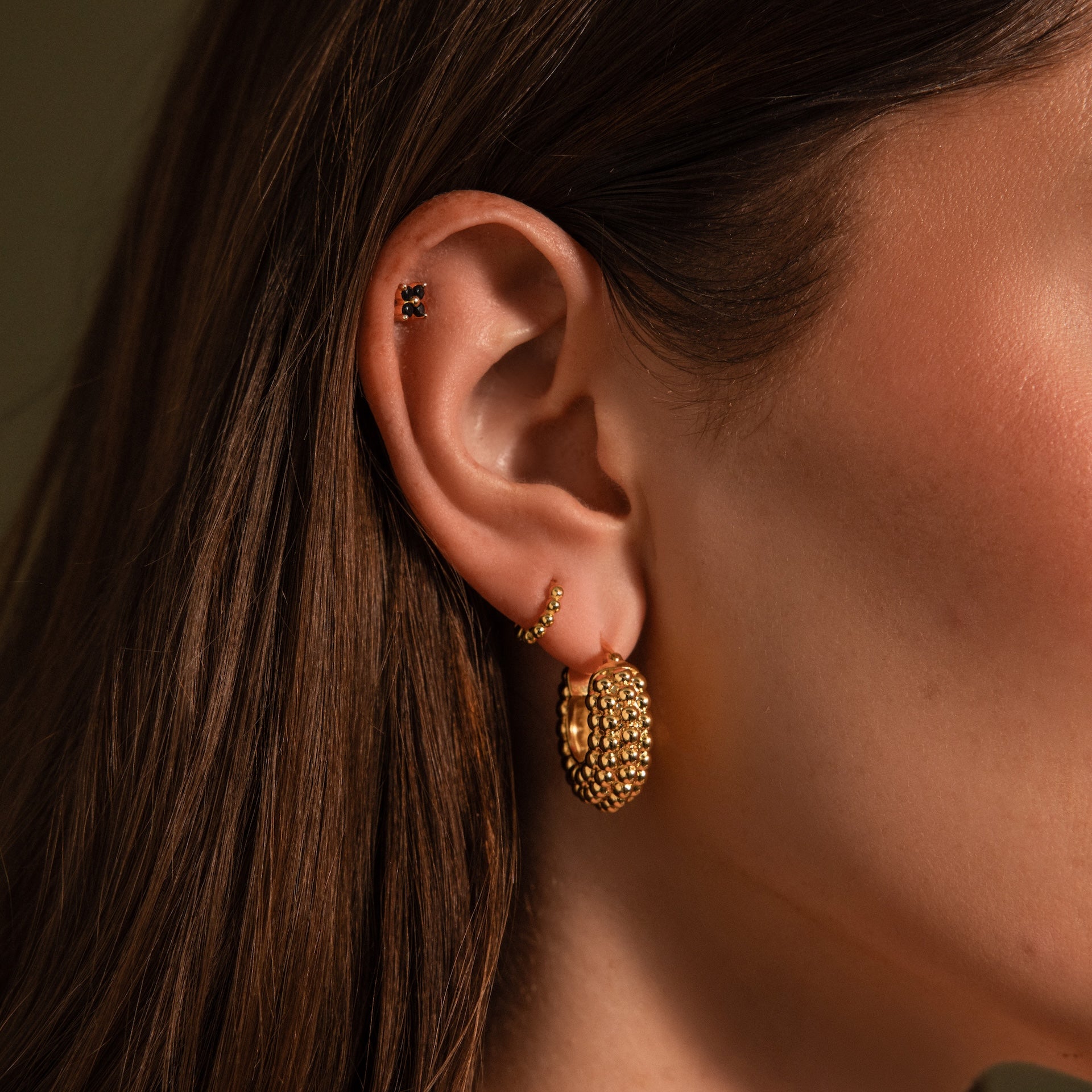 Close-up of a woman's ear adorned with three gold earrings, featuring statement hoops and Beaded Dome Hoops in 18K Gold with delicate beading in varying sizes and textures.