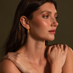 Woman with long brown hair wears Beaded Dome Hoops, posing with arms crossed against a dark background.