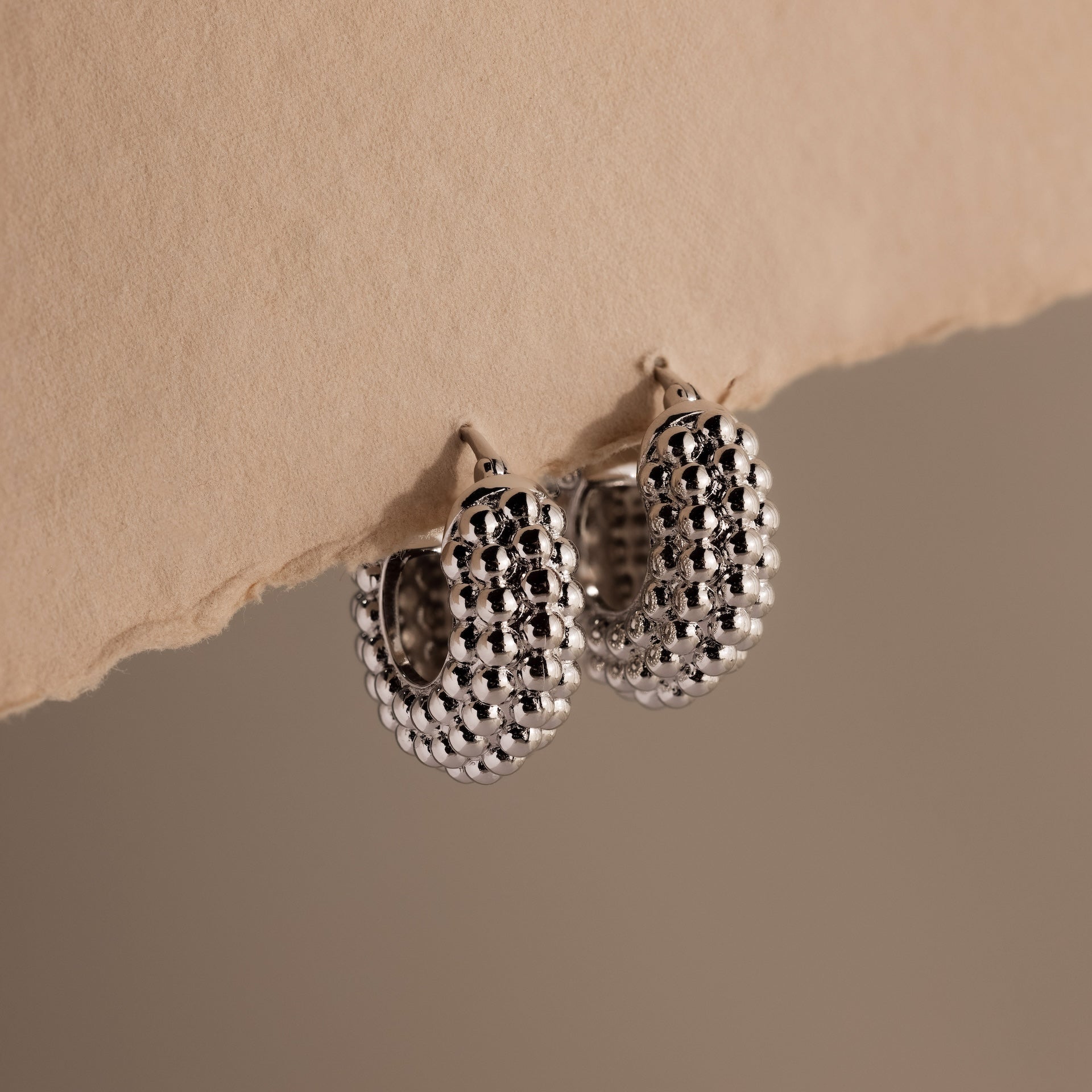 A pair of Beaded Dome Hoops in Silver showcased against torn beige paper.
