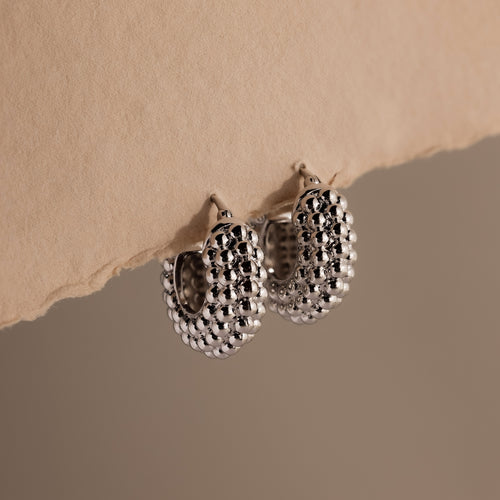 A pair of Beaded Dome Hoops in Silver showcased against torn beige paper.