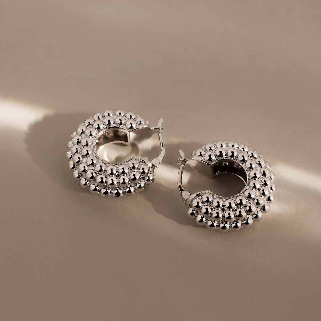 Beaded Dome Hoops in Silver—these statement earrings feature a bold beaded texture, shown on a beige surface with soft lighting for a modern, stylish look.