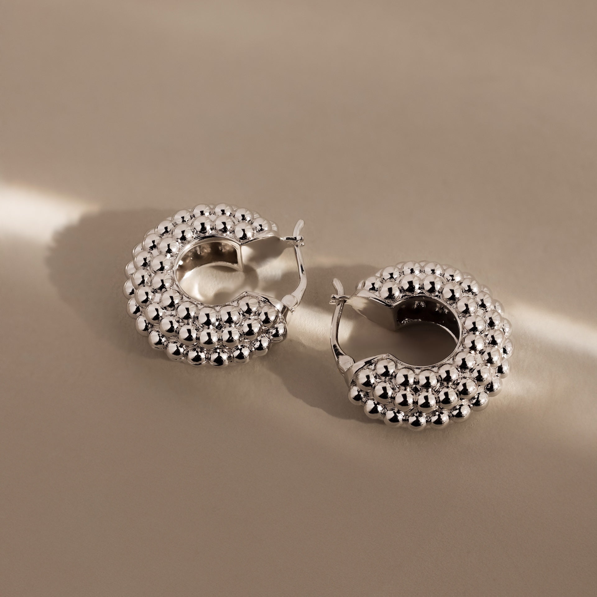 Beaded Dome Hoops in Silver—these statement earrings feature a bold beaded texture, shown on a beige surface with soft lighting for a modern, stylish look.