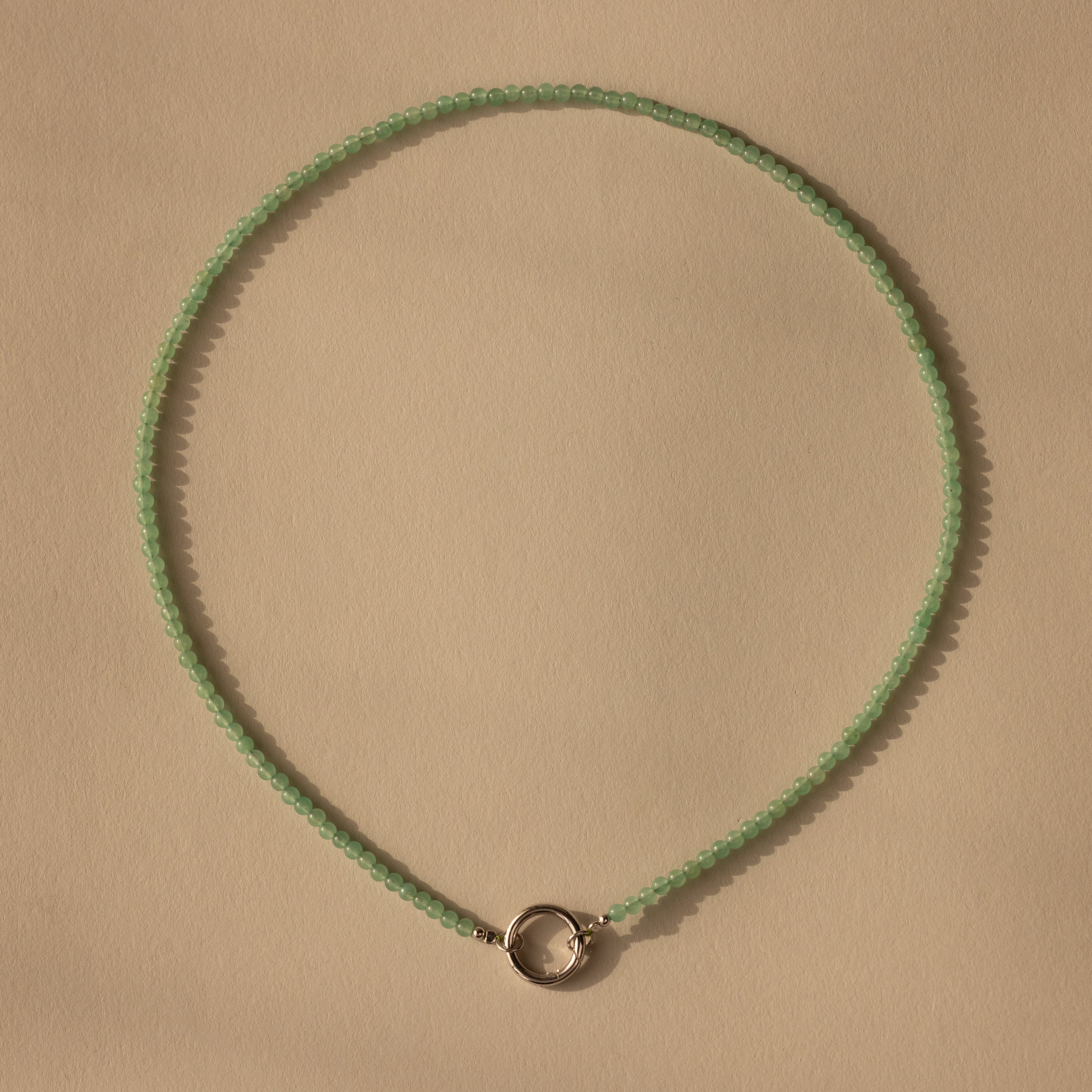 The Beaded Jade Clasp Necklace in Silver, featuring a silver circular clasp, is displayed on a beige background—ideal for adding style as a layering piece.