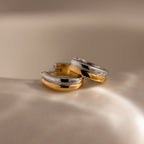 Dainty Mixed Metal Huggies in gold and silver are displayed on a smooth, cream-colored surface under soft lighting—ideal minimalist earrings for lovers of elegant two-tone jewelry.