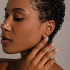 A woman with short curly hair touches her Dainty Mixed Metal Huggies, highlighting smooth skin and natural makeup—an ideal showcase of minimalist jewelry.