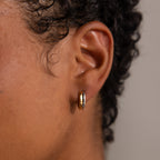 Close-up of a person’s ear wearing Dainty Mixed Metal Huggies with short curly hair, showcasing minimalist jewelry perfect for mixing and matching with gold and silver earrings.