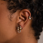 Close-up of an ear with three gold hoops, curly dark hair, and minimalist jewelry—perfect for pairing with our Dainty Mixed Metal Huggies.