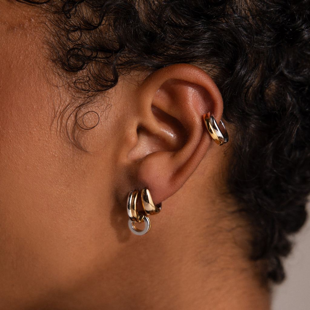 Close-up of an ear wearing three Bold Mixed Metal Huggies in the lobe and a contemporary statement earring in the upper cartilage.