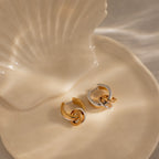The Mixed Metal Circle Hoops—gold and silver interlocking earrings—are elegantly displayed on a cream shell-shaped dish, making them perfect for lovers of versatile jewelry.
