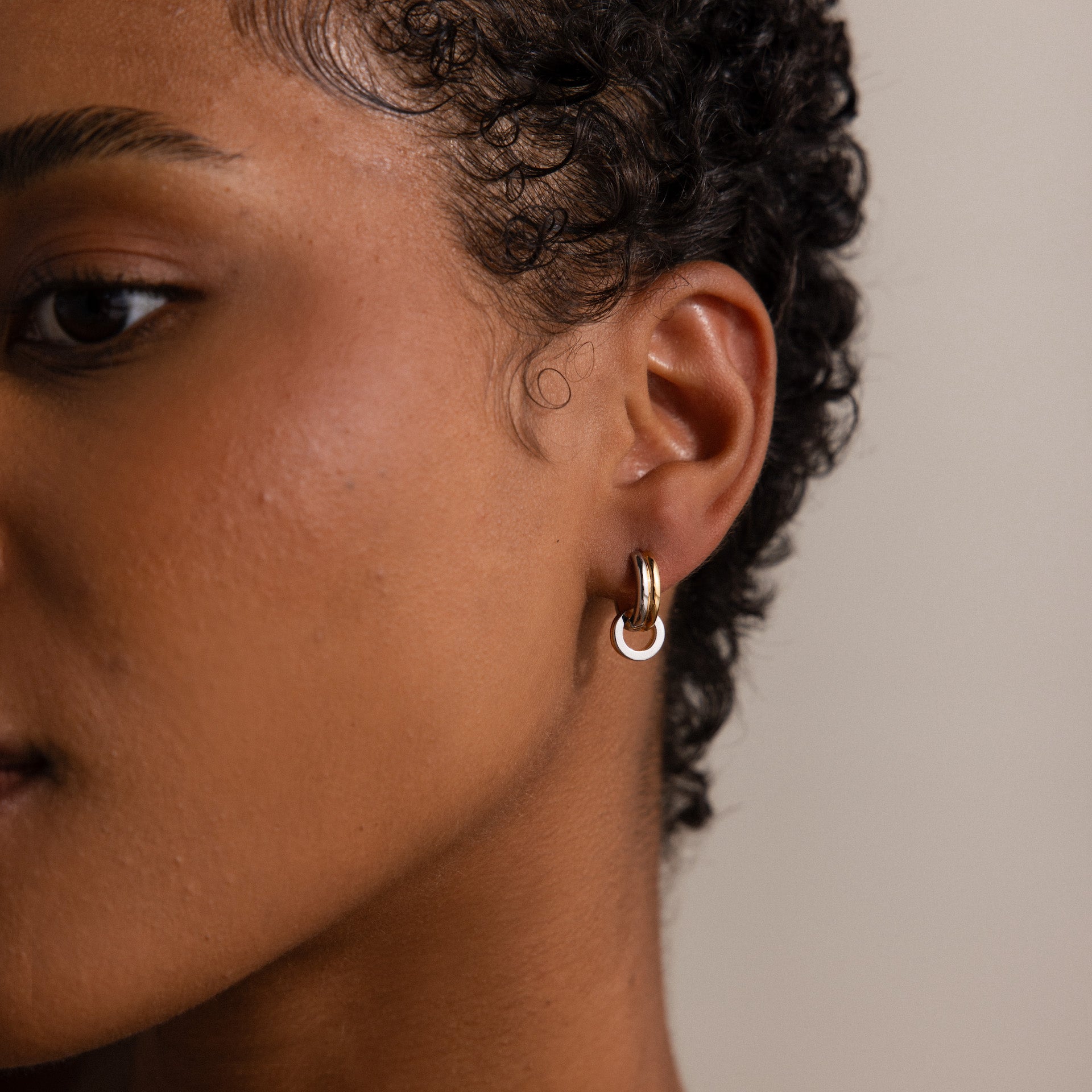 Close-up of a person with short curly hair wearing Mixed Metal Circle Hoops—small, versatile earrings featuring mixed metals and a white accent, ideal for anyone who loves stylish, adaptable jewelry.