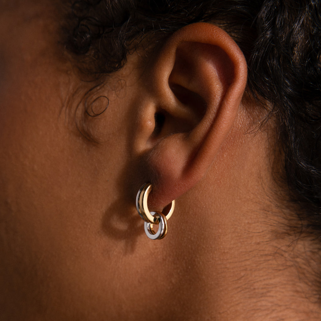 Close-up of an ear wearing Mixed Metal Circle Hoops—two gold and one silver—against brown skin, highlighting the beauty of these versatile earrings for jewelry lovers.