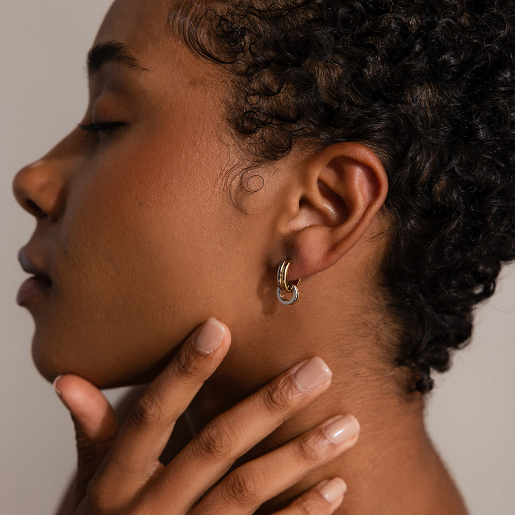 A person with short curly hair wears Mixed Metal Circle Hoops, touching their neck with manicured fingers.