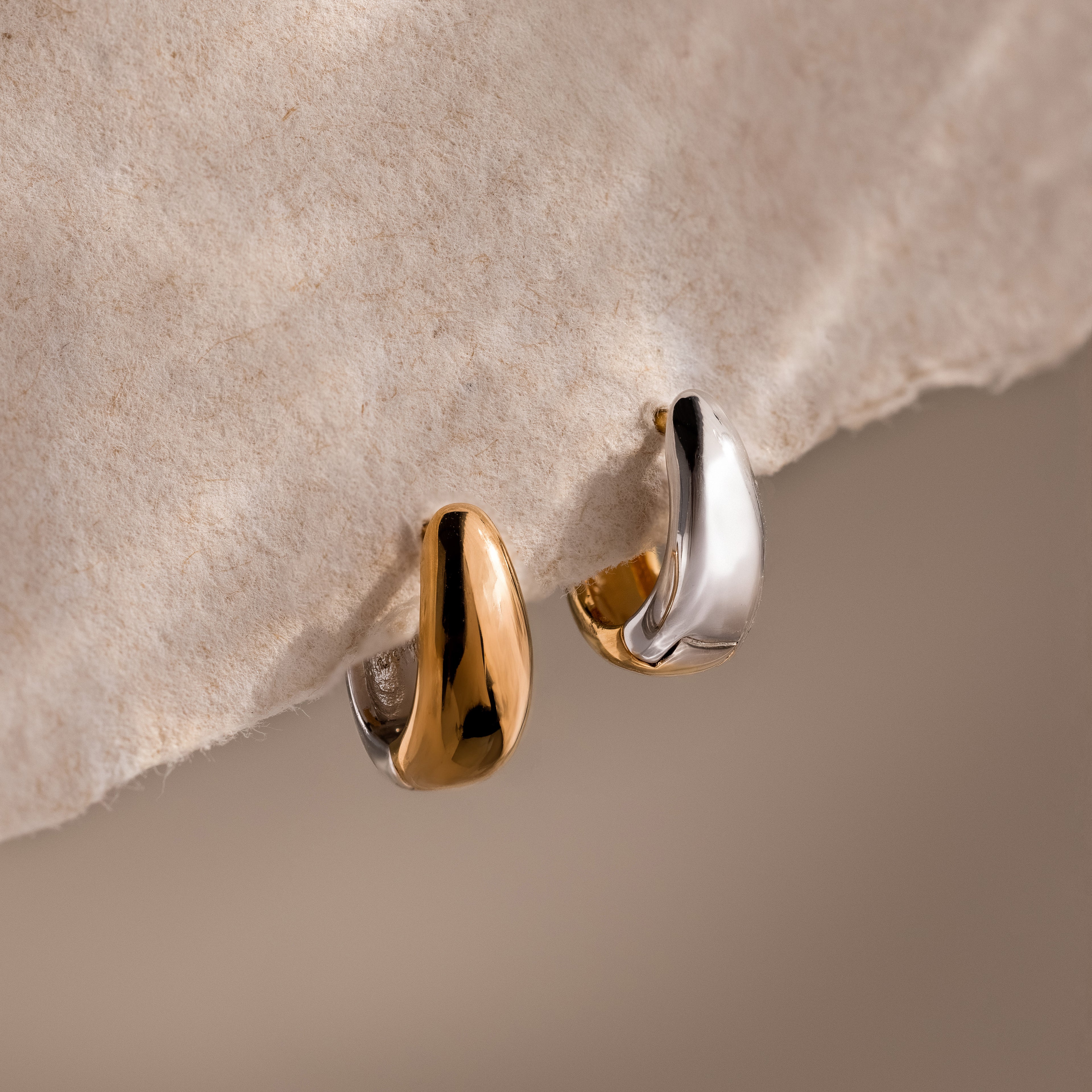 Bold Mixed Metal Huggies—two small, chunky gold and silver earrings—create a contemporary look, shown on textured beige paper.