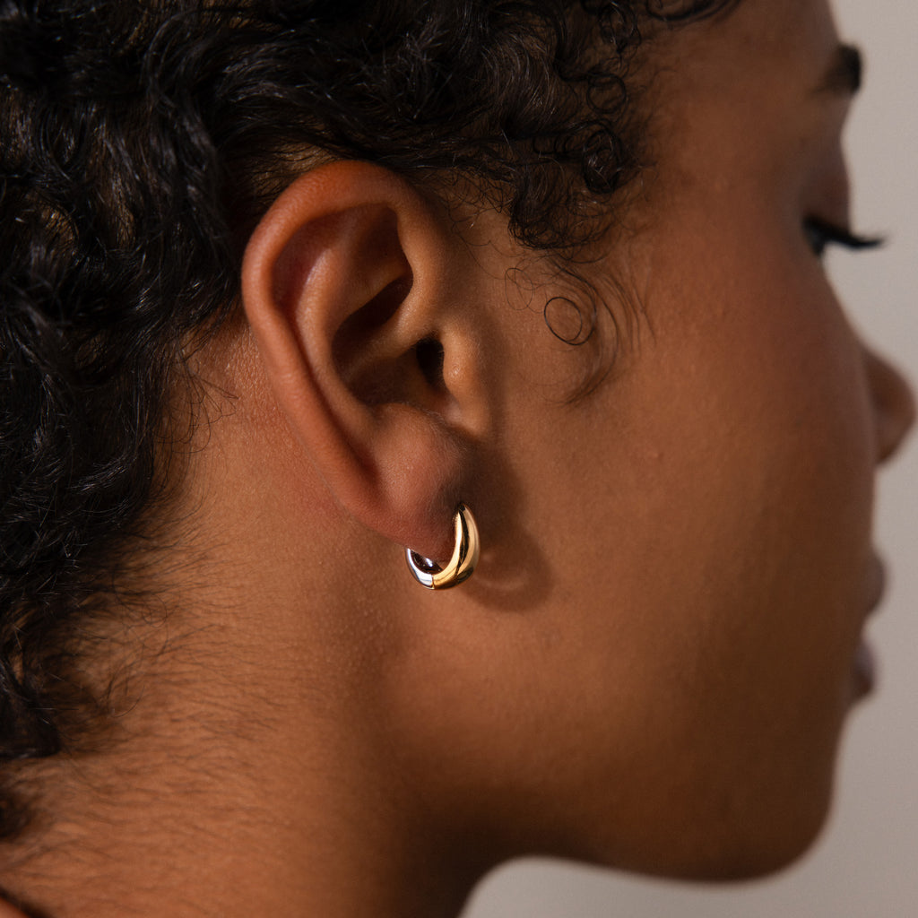 Close-up of a woman's ear with short curly hair, wearing the Bold Mixed Metal Huggies—contemporary statement earrings in delicate gold and silver.