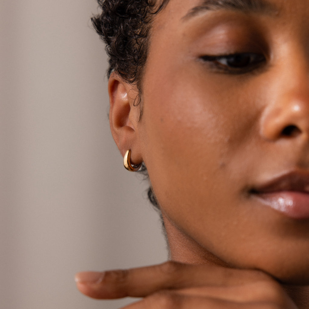 Close-up of a woman’s face with smooth, glowing skin, wearing contemporary statement earrings—a small gold hoop paired with our Bold Mixed Metal Huggies.