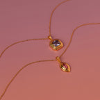 Two Ribbed Alexandrite Pendant Necklaces, each with a vibrant gemstone pendant in purple and pink, are displayed elegantly on a gradient pink background.