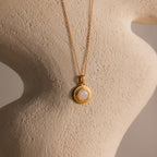 Ribbed Moonstone Pendant Necklace featuring a gold ribbed chain and a round white moonstone pendant, displayed on a textured beige sculpture.