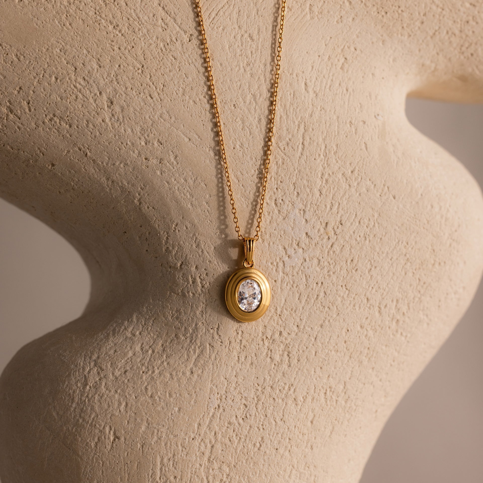 The Ribbed Diamond Pendant Necklace features a vintage-inspired gold ribbed chain with a round diamond pendant, elegantly displayed on a textured beige sculpture.