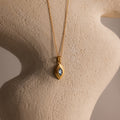The Ribbed Aquamarine Pendant Necklace is showcased on a textured, curved beige sculpture.