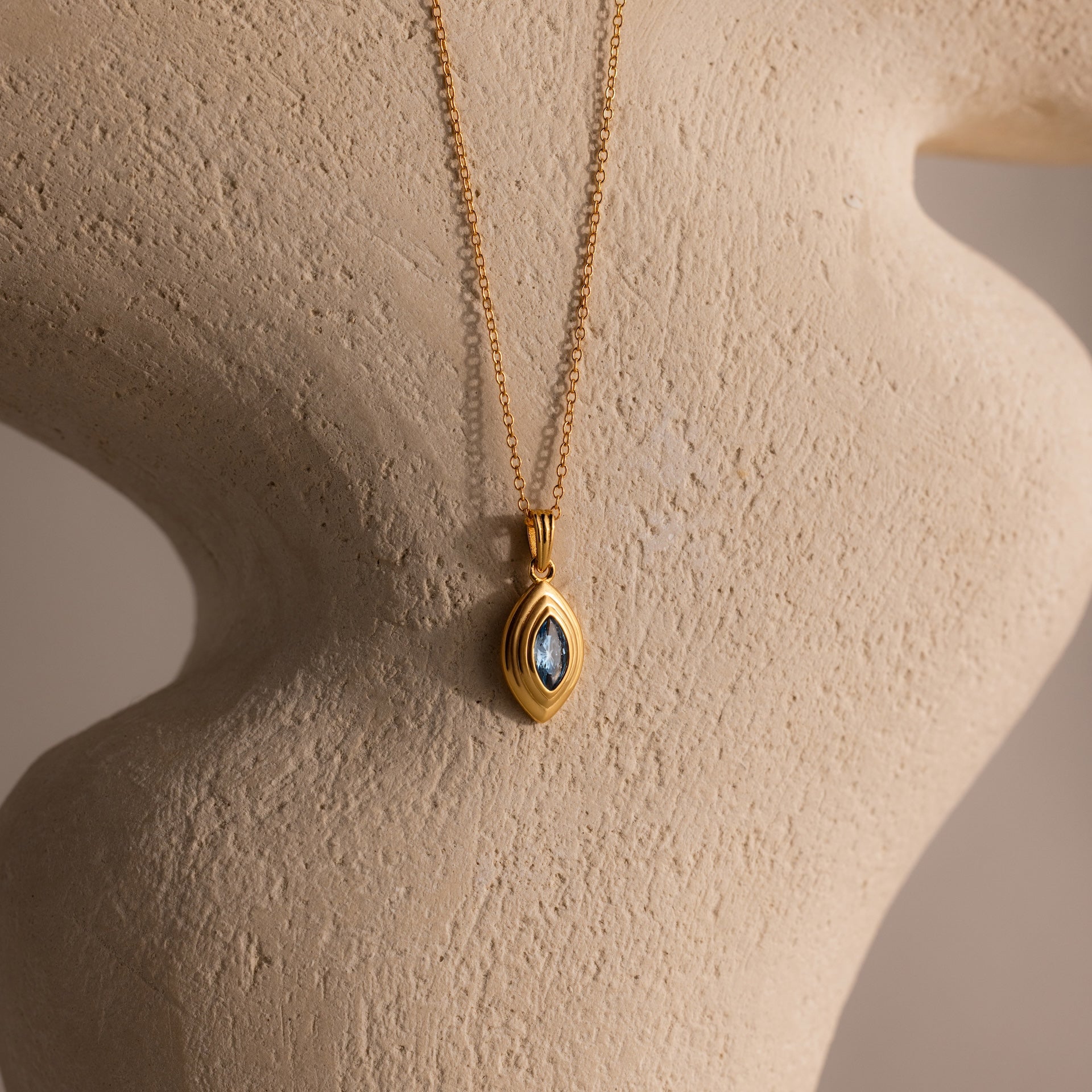 The Ribbed Aquamarine Pendant Necklace is showcased on a textured, curved beige sculpture.