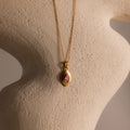 The Ribbed Pink Tourmaline Pendant Necklace is displayed on a textured beige sculpture background.