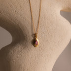 The Ribbed Pink Tourmaline Pendant Necklace is displayed on a textured beige sculpture background.