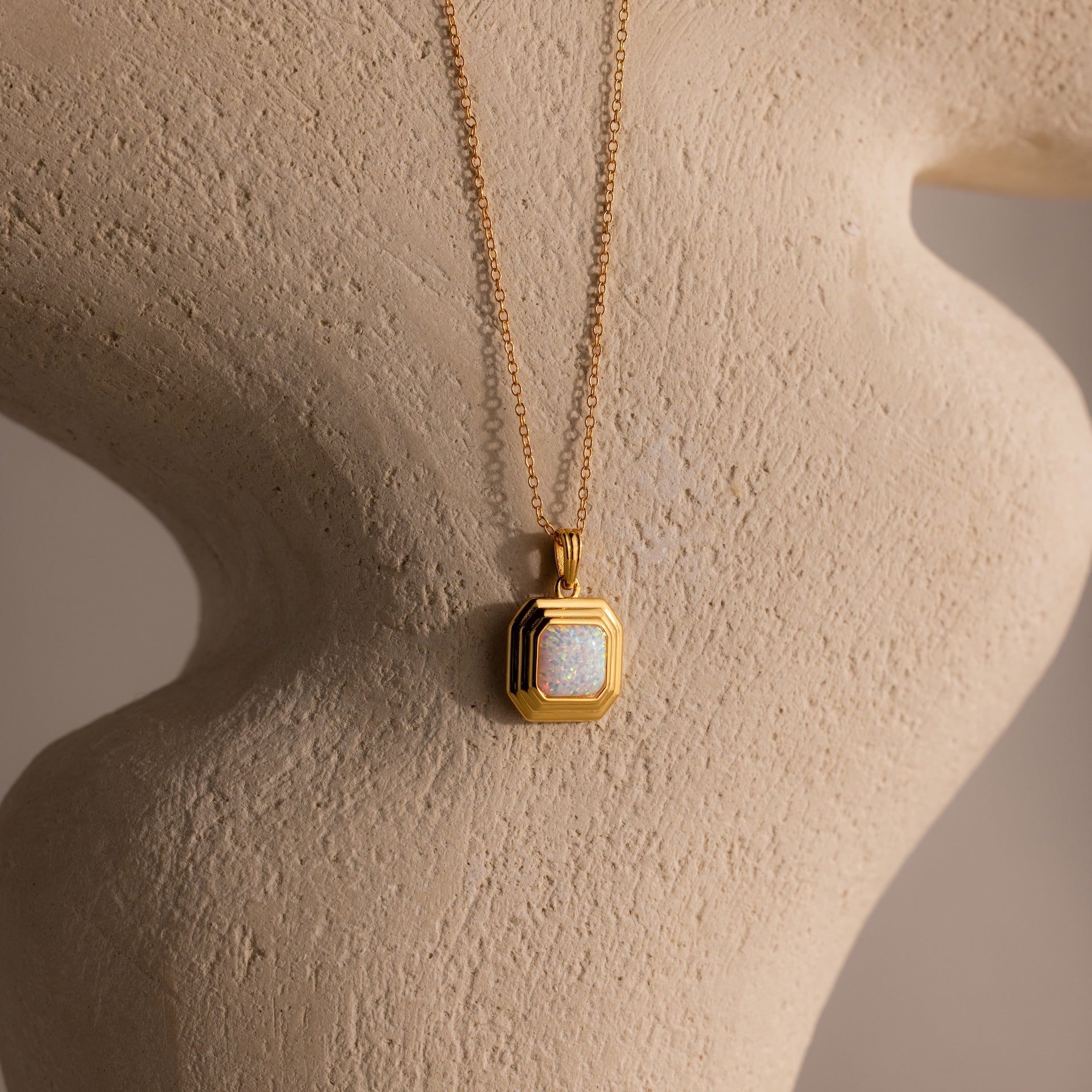 The Ribbed Opal Pendant Necklace is showcased against a textured beige sculpture backdrop.