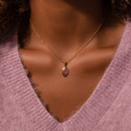 The Ribbed Pink Tourmaline Pendant Necklace shines elegantly on a person dressed in a soft, light purple V-neck sweater.