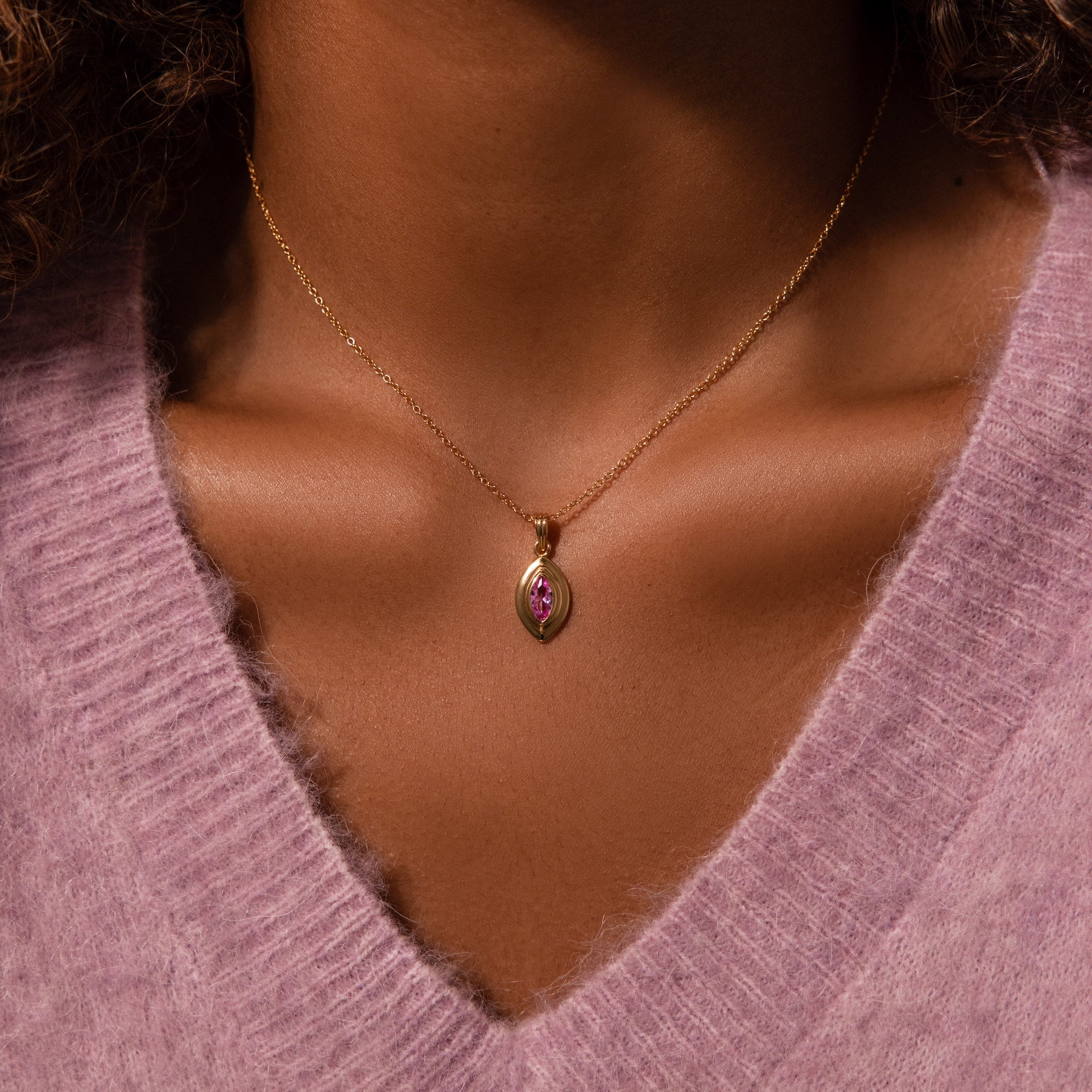 Close-up of a person wearing the Ribbed Garnet Pendant Necklace, featuring a gold chain and pink pendant, styled with a soft pink sweater.