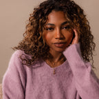 Woman with curly hair wearing a fuzzy lavender sweater and a Ribbed Pink Tourmaline Pendant Necklace, looking at the camera.