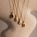 Four Ribbed Birthstone Pendant Necklaces with colorful gemstones are showcased on a textured beige sculpture, each featuring a vintage-inspired ribbed gold design.