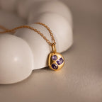 Mixed Amethyst Capsule Pendant Necklace featuring three purple gemstones, displayed on a smooth white surface under soft, warm lighting.