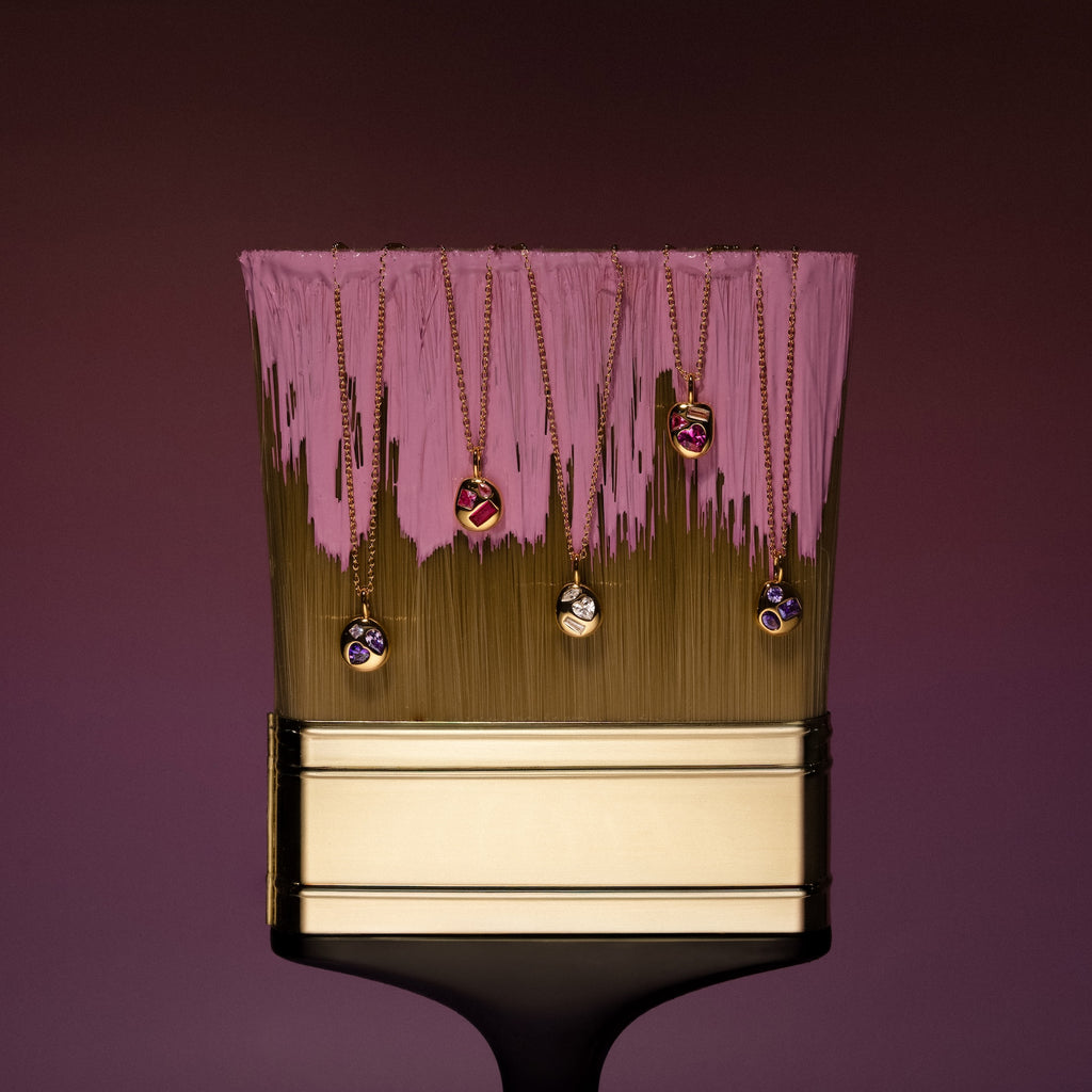 A gold paintbrush with pink paint, displaying several gold necklaces, including the Mixed Topaz Capsule Pendant Necklace and other vibrant gemstone pendants.