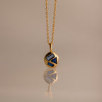 Mixed Sapphire Capsule Pendant Necklace featuring a gold round capsule pendant with geometric blue sapphire inlays, displayed on a neutral background.
