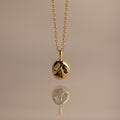 Mixed Peridot Capsule Pendant Necklace with a round pendant featuring geometric shapes, reflected on a smooth surface.