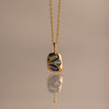 Mixed Blue Zircon Capsule Pendant Necklace, featuring three uniquely shaped blue zircons in a capsule pendant, reflected on a smooth surface.