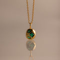 Mixed Emerald Capsule Pendant Necklace featuring green gemstones in a capsule-shaped pendant, elegantly reflected on a smooth surface.