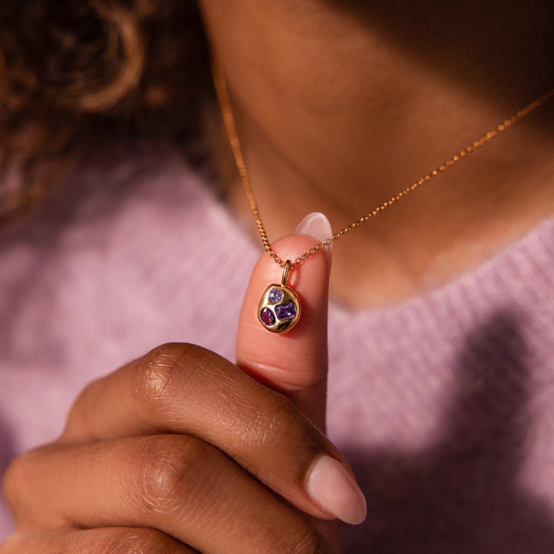 A person holds a Mixed Birthstone Capsule Necklace with a gemstone pendant while wearing a lavender sweater.
